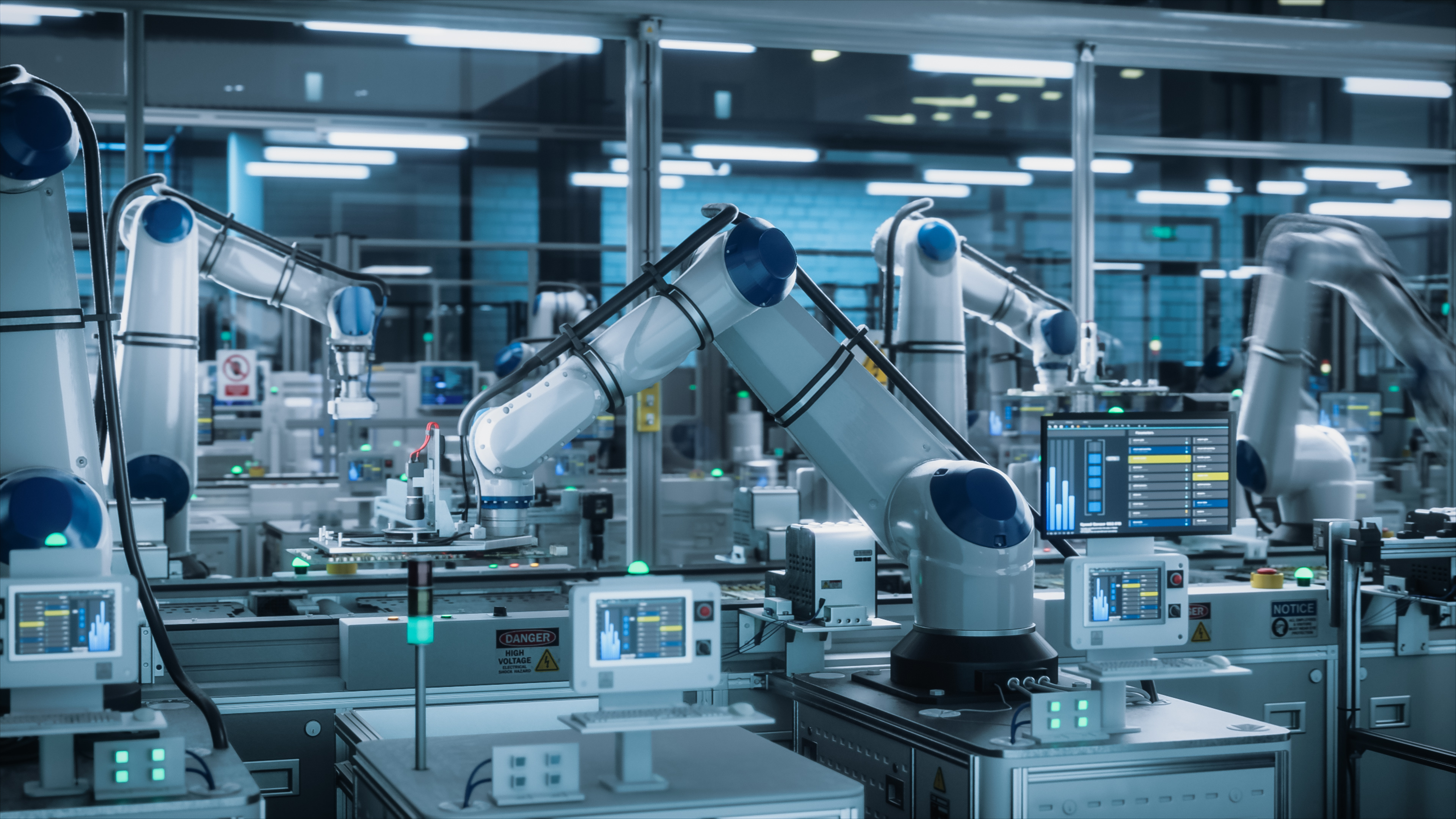 Robotic arms working along an automated production line, with control screens and status lights down the bench.